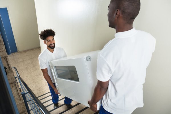 Close-up Of Two Male Young Movers Carrying White Cabinet While Climbing Steps At Home