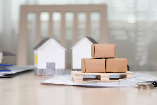 Pallet with carton boxes in front of small paper houses. Closeup